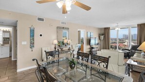 A spacious living room with a glass dining table, a ceiling fan, and a view of the city. - Terrace At Pelican Beach 401 3 Bedroom Home (Destin)