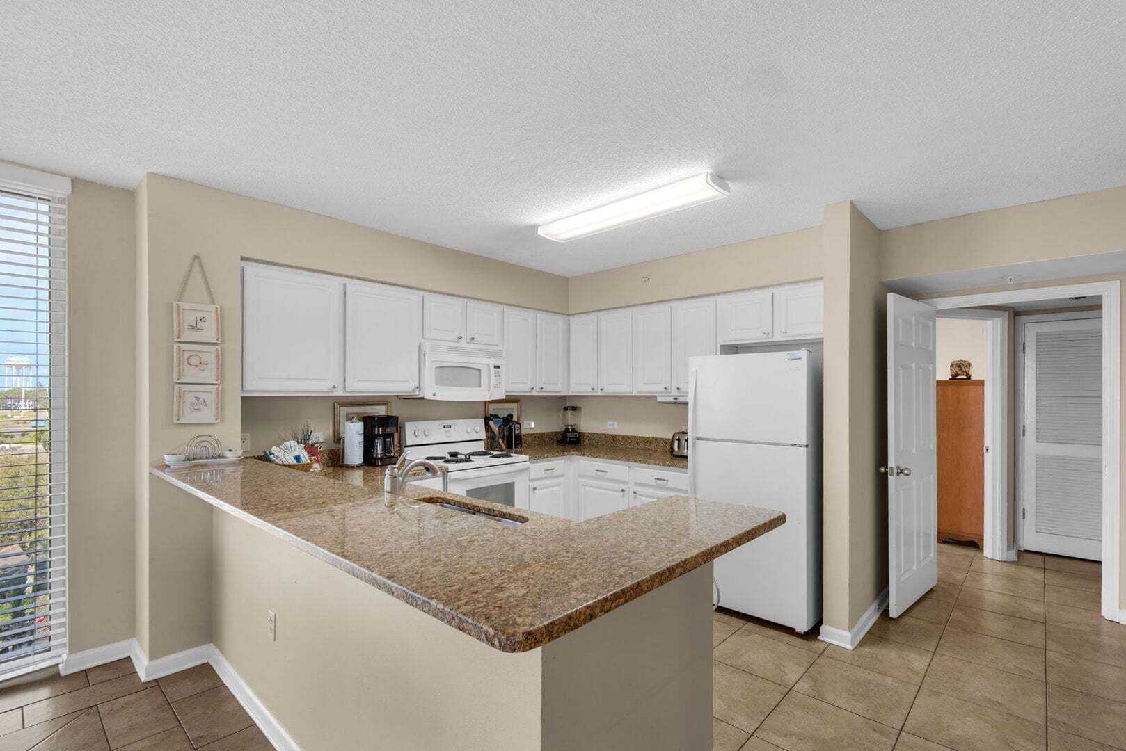 A kitchen with white cabinets, a granite countertop, a stove, a microwave, and a refrigerator.