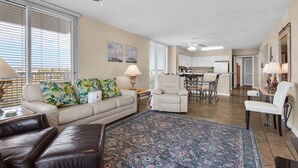 A spacious living room with a large rug, a sofa, a coffee table, and a dining area with a table and chairs. - Terrace At Pelican Beach 401 3 Bedroom Home (Destin)