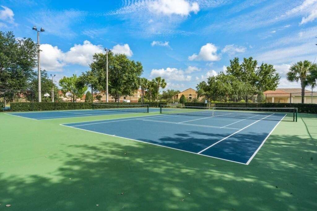 A tennis court with a net, surrounded by trees and buildings.