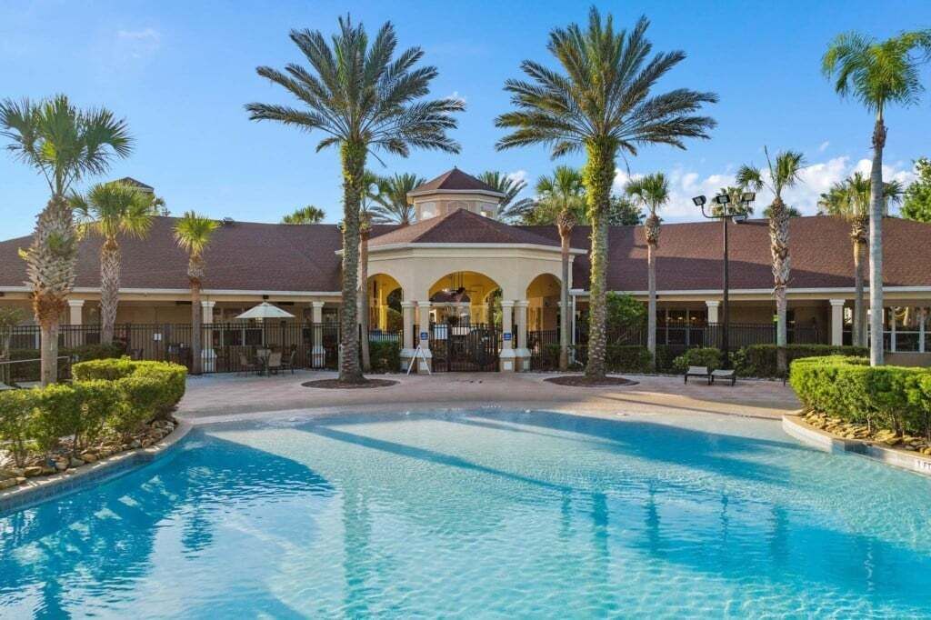 A hotel with a swimming pool, palm trees, and a covered outdoor area.