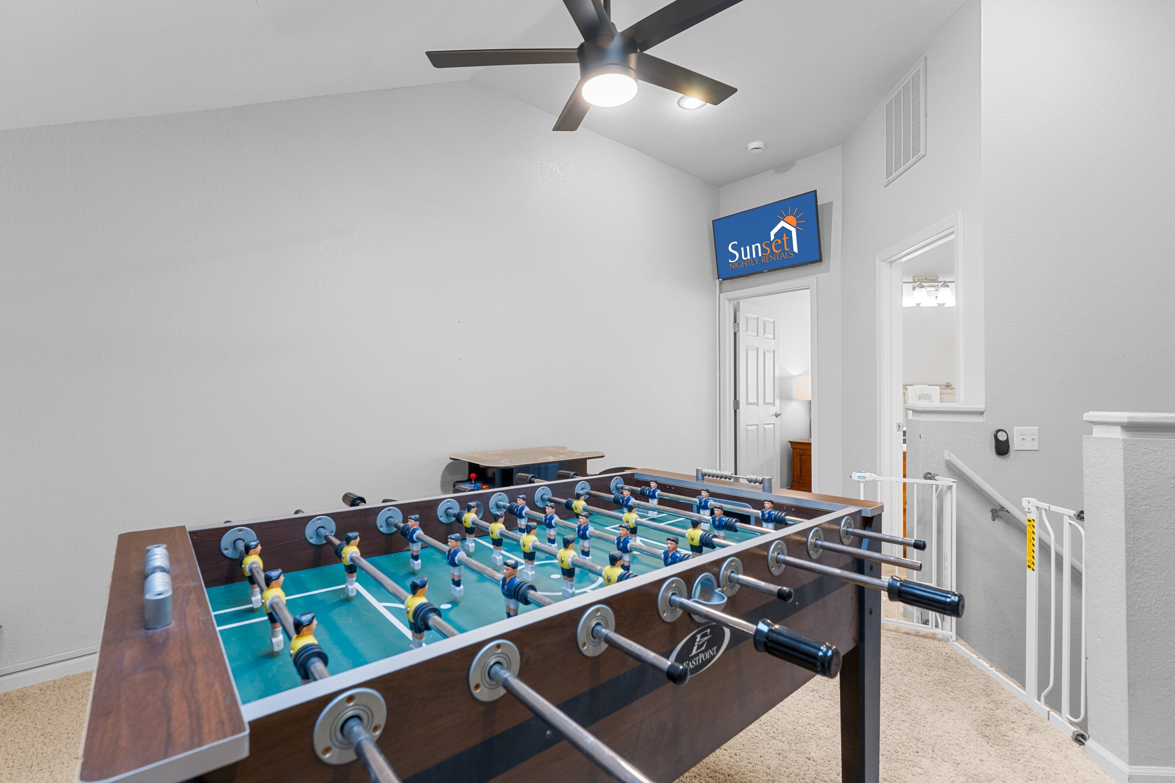 A room with a foosball table, a ceiling fan, and a sign that says 'Sunso'.