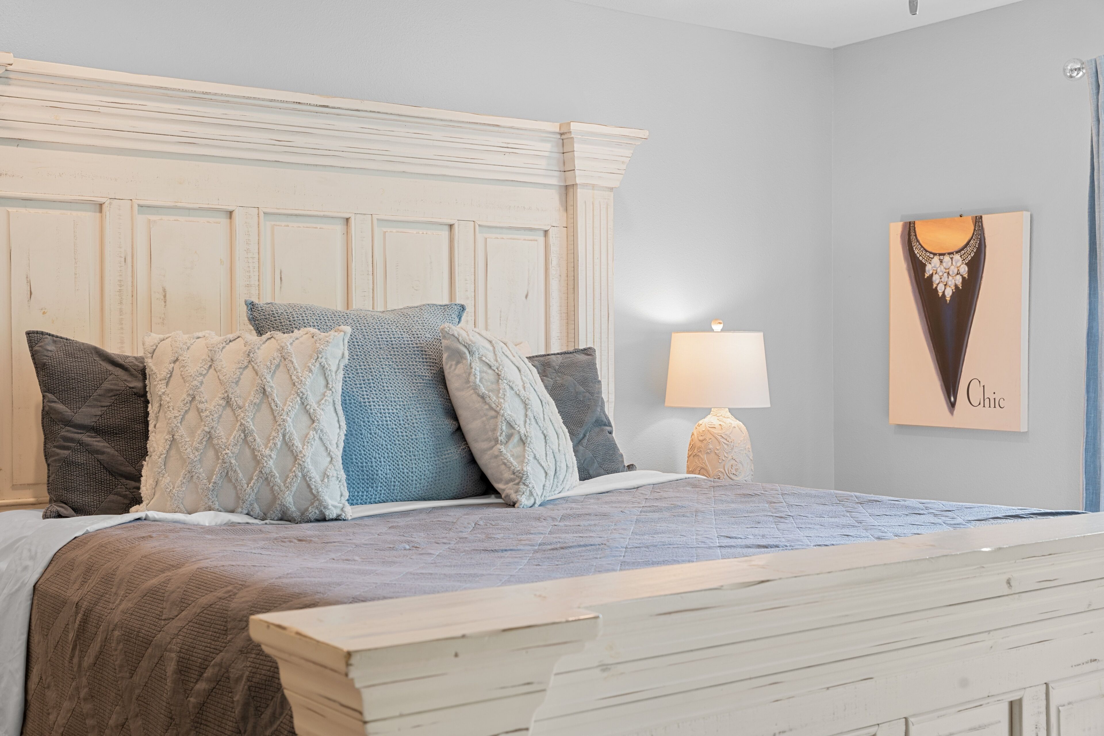 A bedroom with a bed, pillows, a nightstand, a lamp, and a wall art piece.