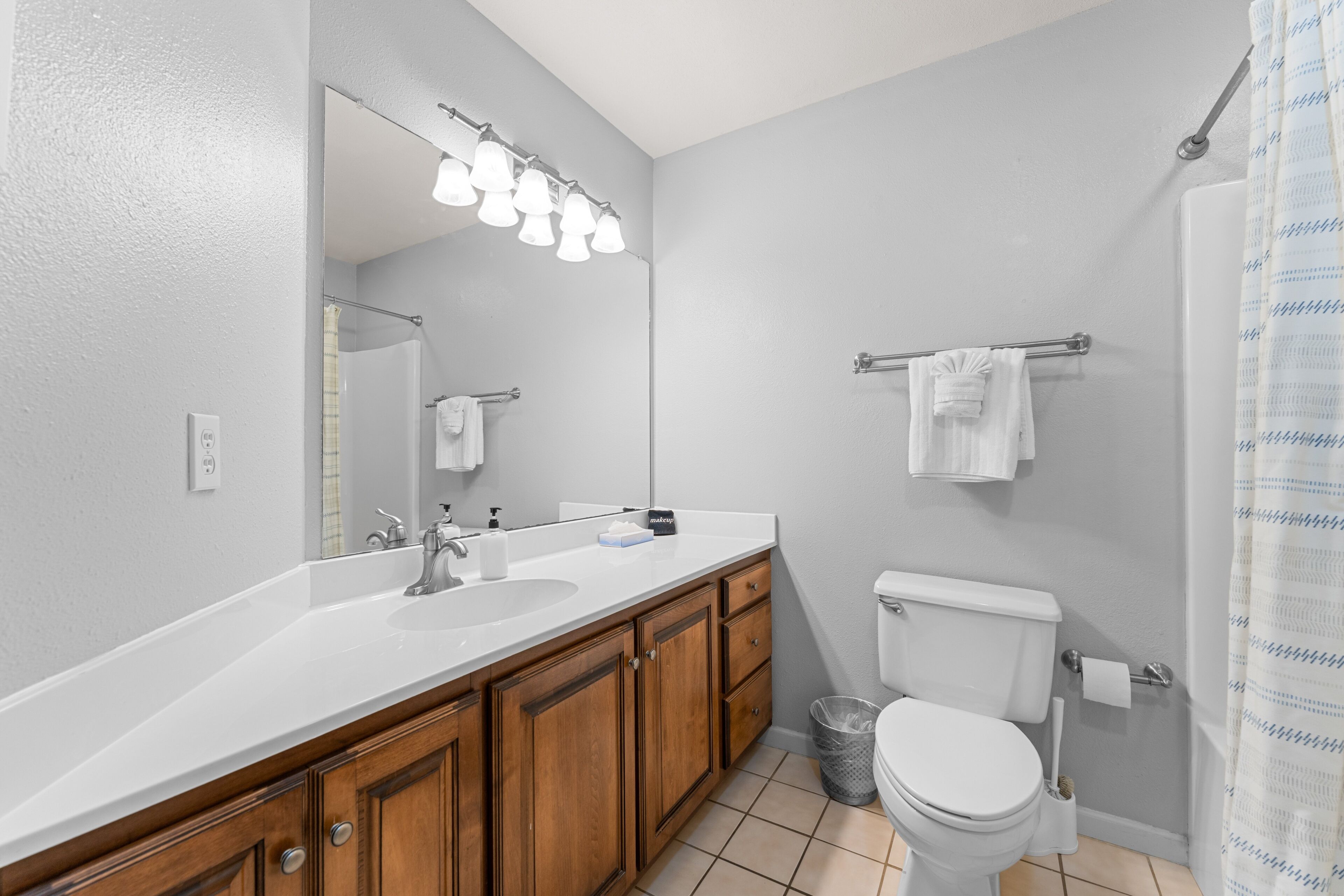 A bathroom with a white sink, wooden cabinets, a toilet, and a shower curtain.