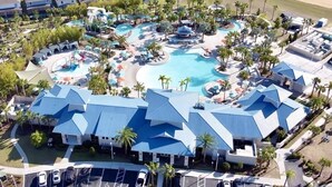 Ett flygbildsfoto av ett semesterområde med flera pooler, en stor byggnad med ett blått tak och ett område med strand.