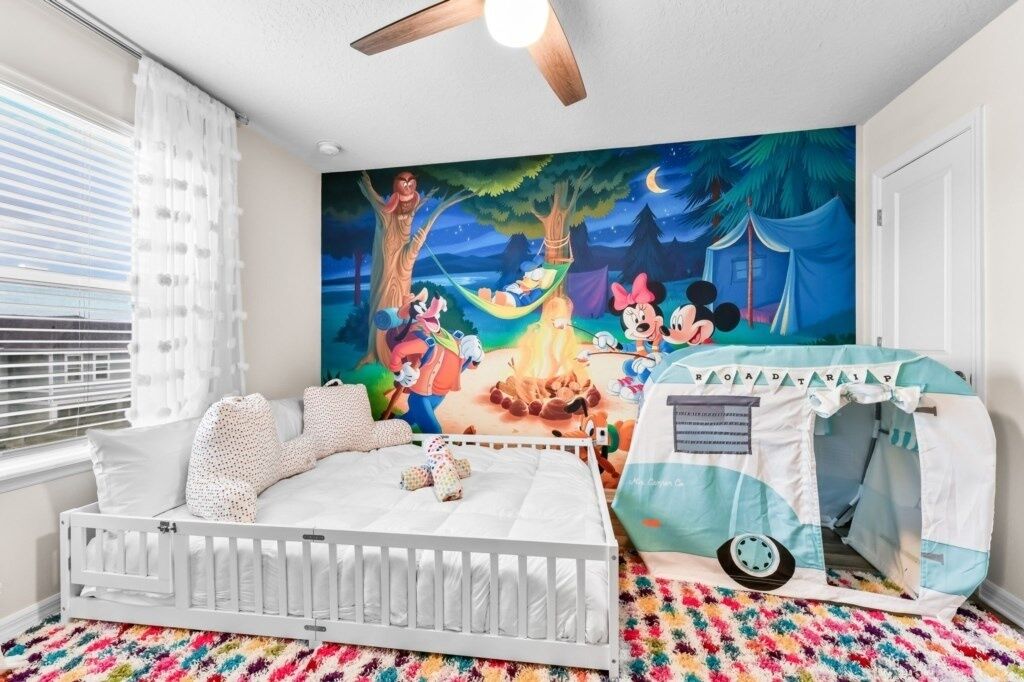 Een kinderkamer met een ledikant, een tentje en een muurschildering van Disney-personages.