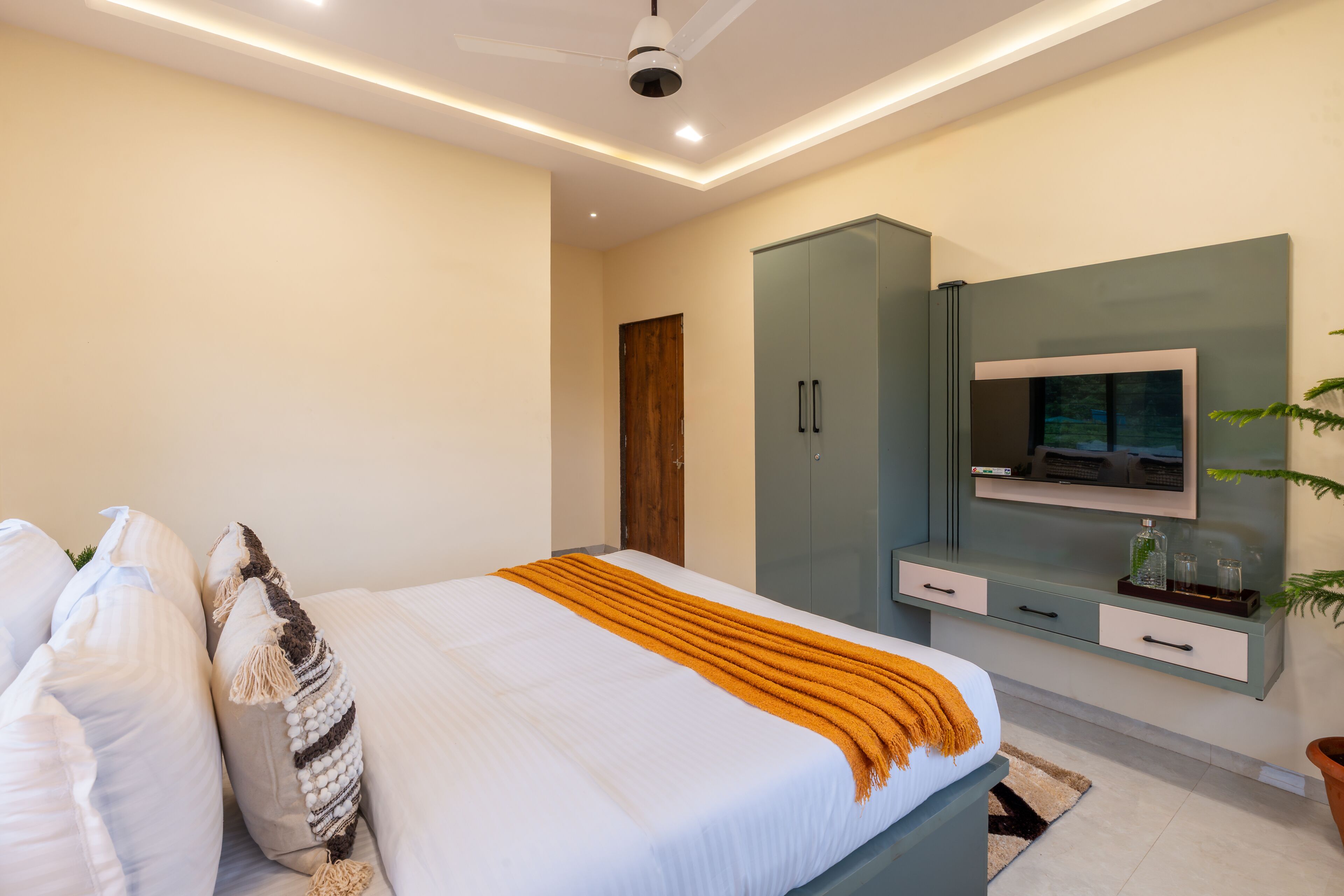 A modern bedroom with a bed, a television, a wardrobe, and a ceiling fan.