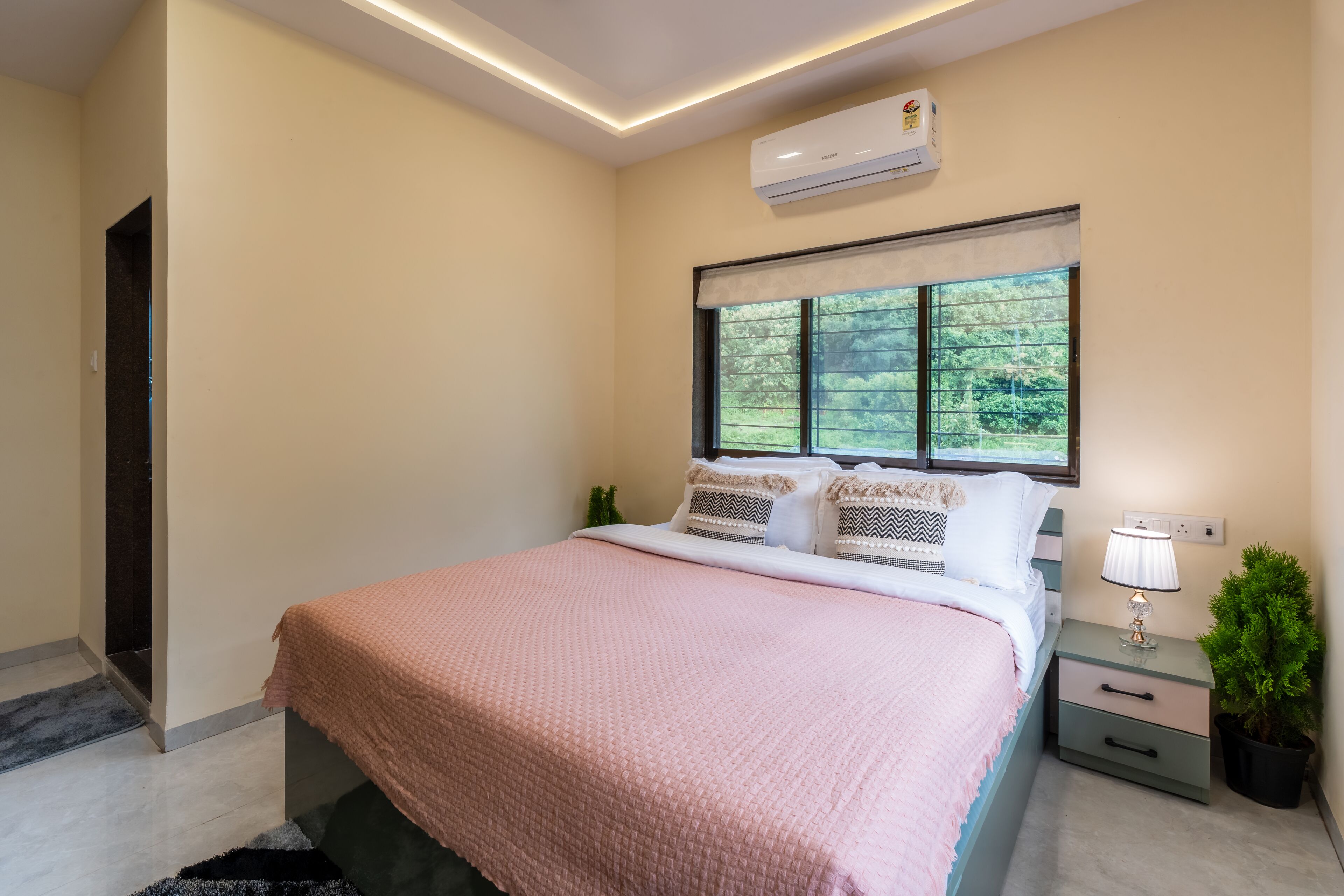 Une chambre à coucher avec un lit, une table de chevet, une lampe, une plante en pot et une fenêtre donnant sur un beau paysage.