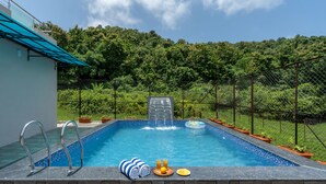 Ein Swimmingpool mit Wasserfall, umgeben von einem Zaun und Kübelpflanzen.