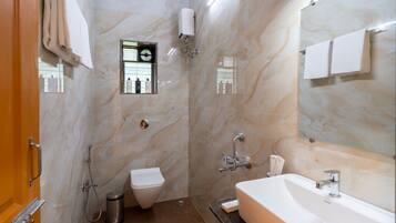 A bathroom with a marble wall, a sink, a toilet, and a shower.