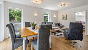 Een moderne woonkamer met een eettafel, grijze gestoffeerde fauteuils, een bank en een plafondlamp.