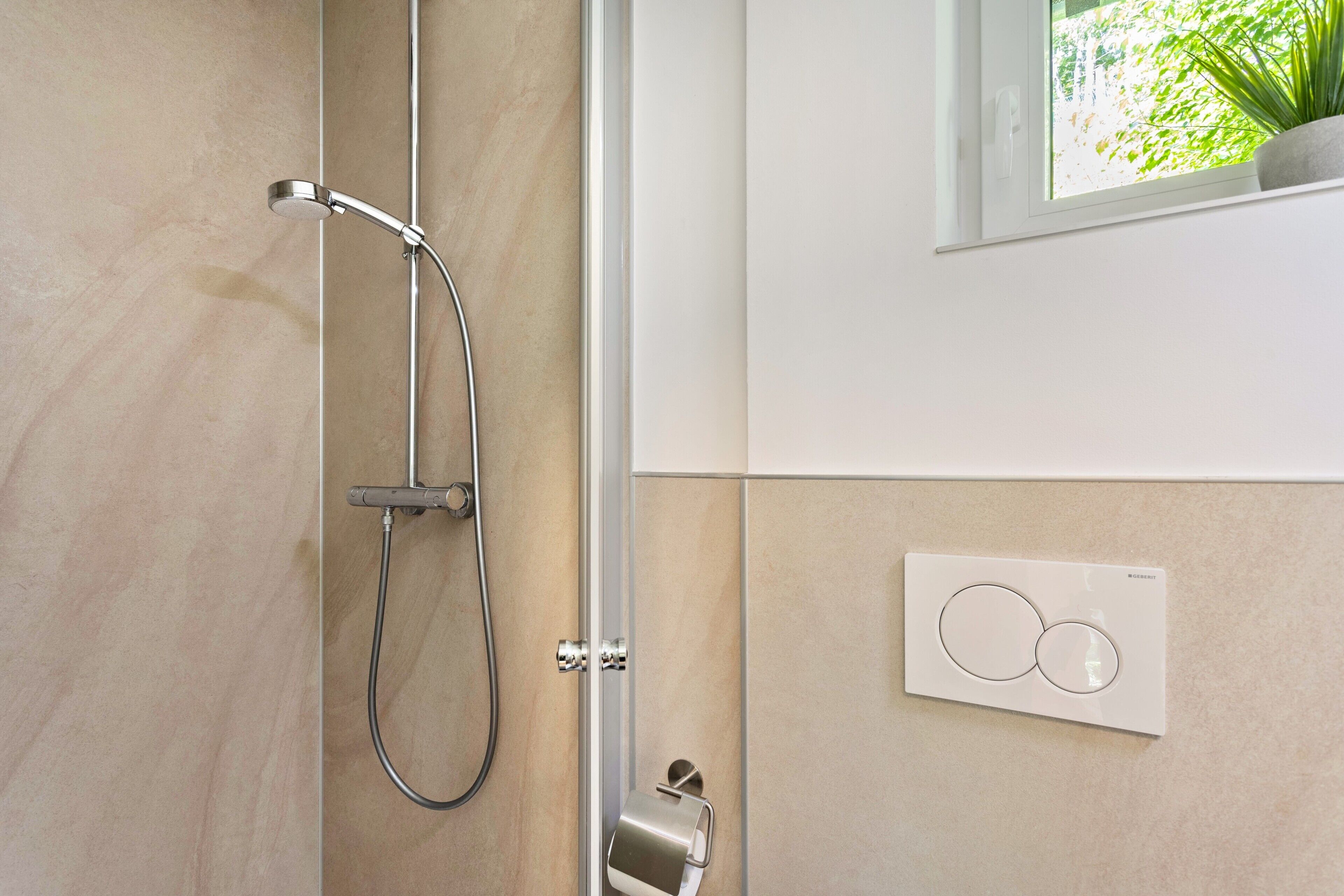 A modern bathroom with a shower, a toilet paper holder, and a thermostat on the wall.