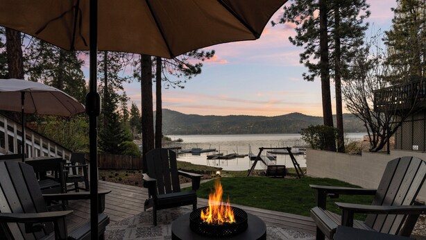 A deck with a fire pit, outdoor furniture, and a view of a lake with boats. - Lakefront Escape with Private Dock, Hot Tub, AC, EV charger, & Game Room (Big Bear Lake)