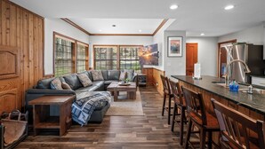 A modern kitchen with a built-in island, wooden flooring, and a large window with blinds. - Lakefront Escape with Private Dock, Hot Tub, AC, EV charger, & Game Room (Big Bear Lake)