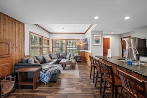 A modern kitchen with a built-in island, wooden flooring, and a large window with blinds.