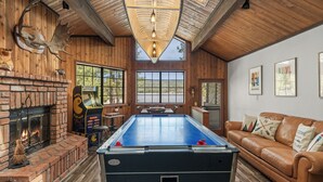 A pool table in a room with wooden walls, a fireplace, and a leather couch. - Lakefront Escape with Private Dock, Hot Tub, AC, EV charger, & Game Room (Big Bear Lake)
