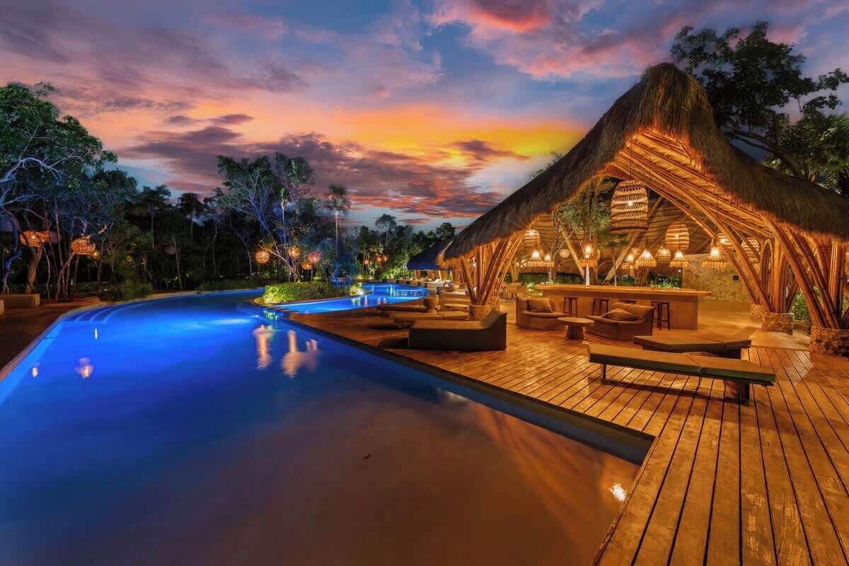 A poolside area with a thatched-roof structure, wooden deck, and lounge seating.