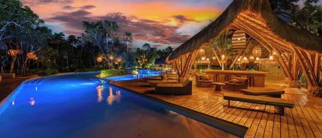 A poolside area with a thatched-roof structure, wooden deck, and lounge seating.