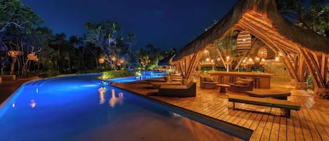 A poolside area with a wooden deck, a thatched-roof structure, and outdoor seating.