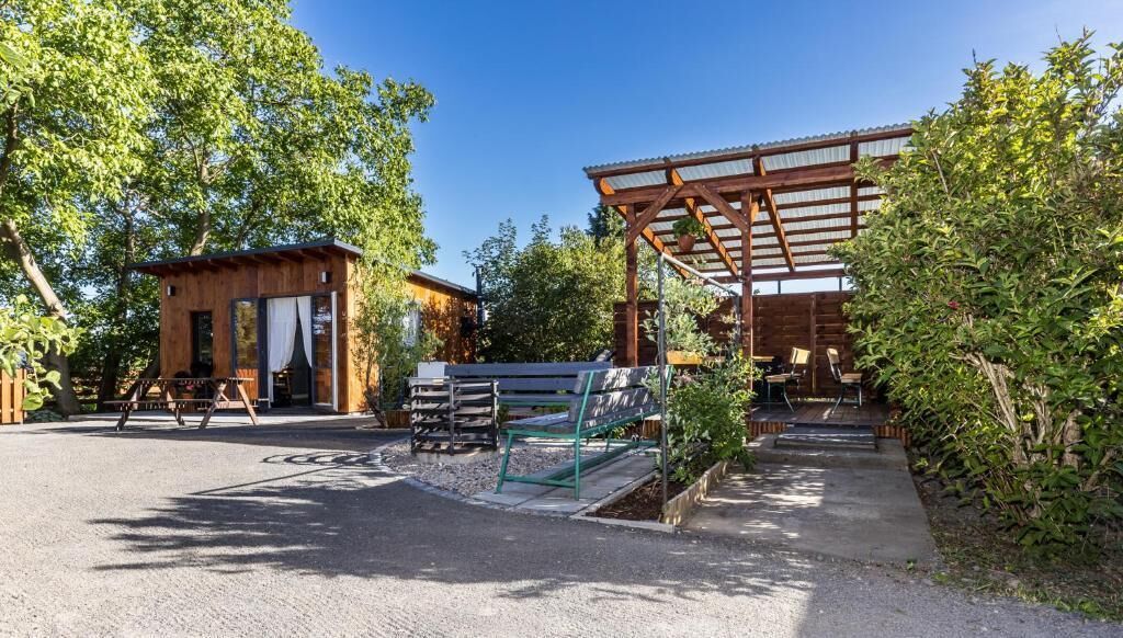 A wooden cabin with a covered outdoor seating area, surrounded by trees.