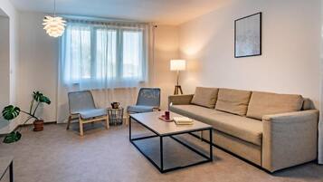 A living room with a sofa, two chairs, a coffee table, a lamp, a potted plant, and a window with curtains.