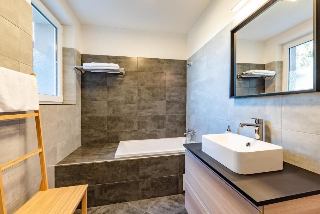 Une salle de bain moderne avec une baignoire, un grand miroir et un banc en bois.