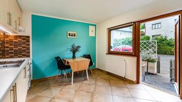 Una cocina con pared verde azulado, una mesa de comedor con sillas y una ventana con vistas a un jardín.