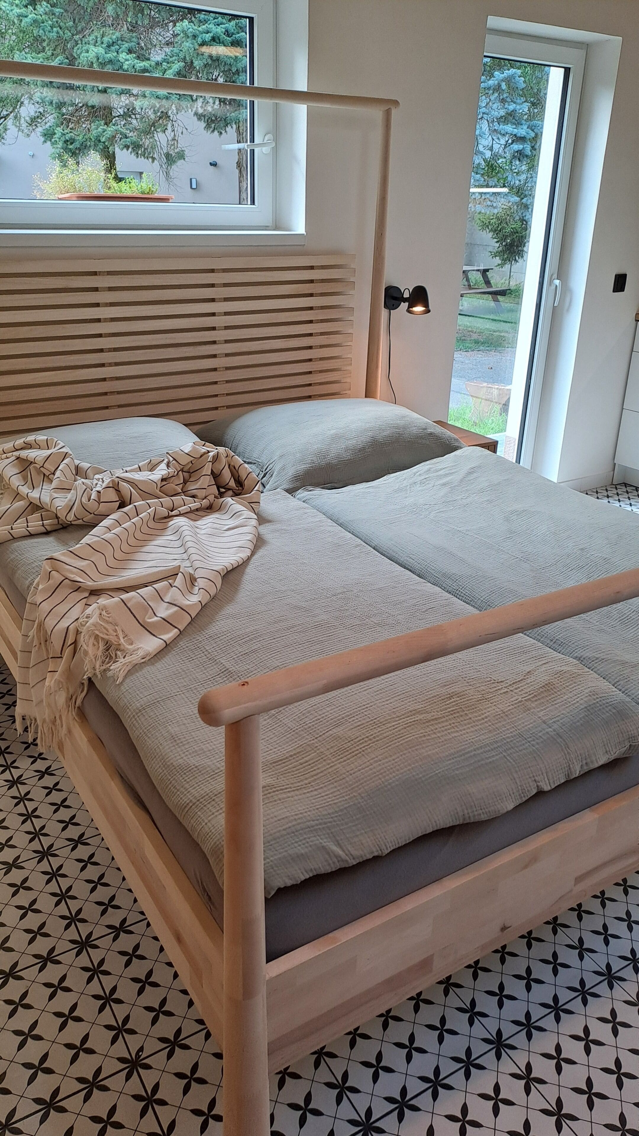 Een bed met houten frame, hoofdbord met horizontale latten en een vloer met patroon.