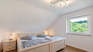 A bedroom with a wooden bed, bedside tables, a nightstand, a window with a view of greenery, and a ceiling light fixture. - Rural, Quiet Apartment (Rosengarten)