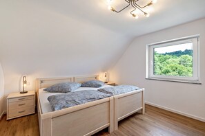 A bedroom with a wooden bed, bedside tables, a nightstand, a window with a view of greenery, and a ceiling light fixture. - Rural, Quiet Apartment (Rosengarten)