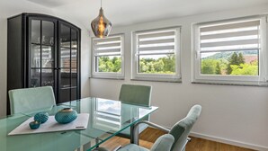 A modern room with a glass table, chairs, a black cabinet, and large windows with a view of greenery. - Rural, Quiet Apartment (Rosengarten)