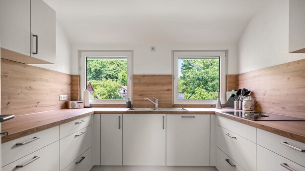 A modern kitchen with white cabinets, a wooden countertop, and a large window providing a view of greenery outside. - Rural, Quiet Apartment (Rosengarten)