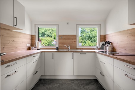 A modern kitchen with white cabinets, a wooden countertop, and a large window providing a view of greenery outside.. Rural, Quiet Apartment