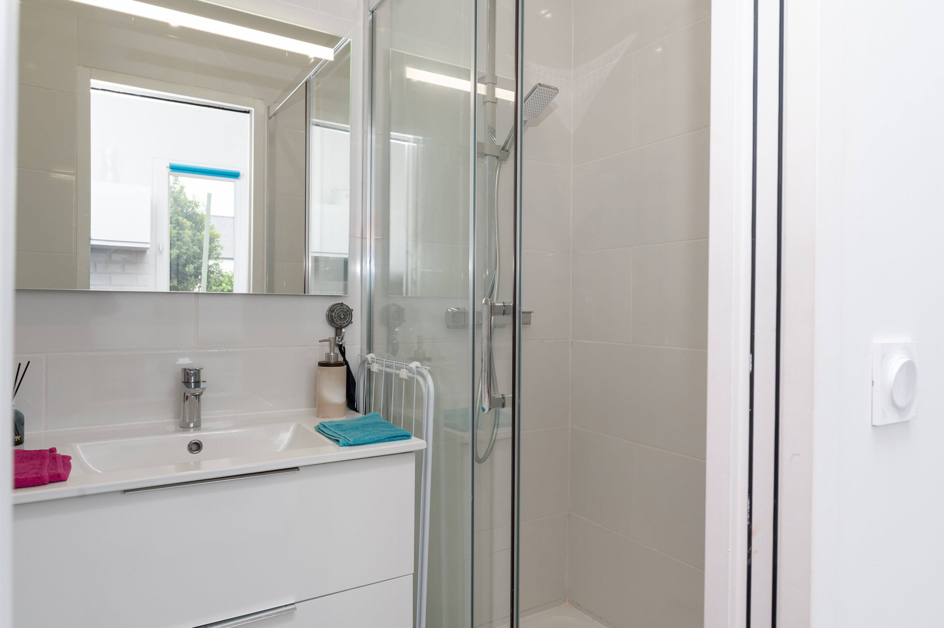 A modern bathroom with a glass shower enclosure, a white sink, and a mirror above it.