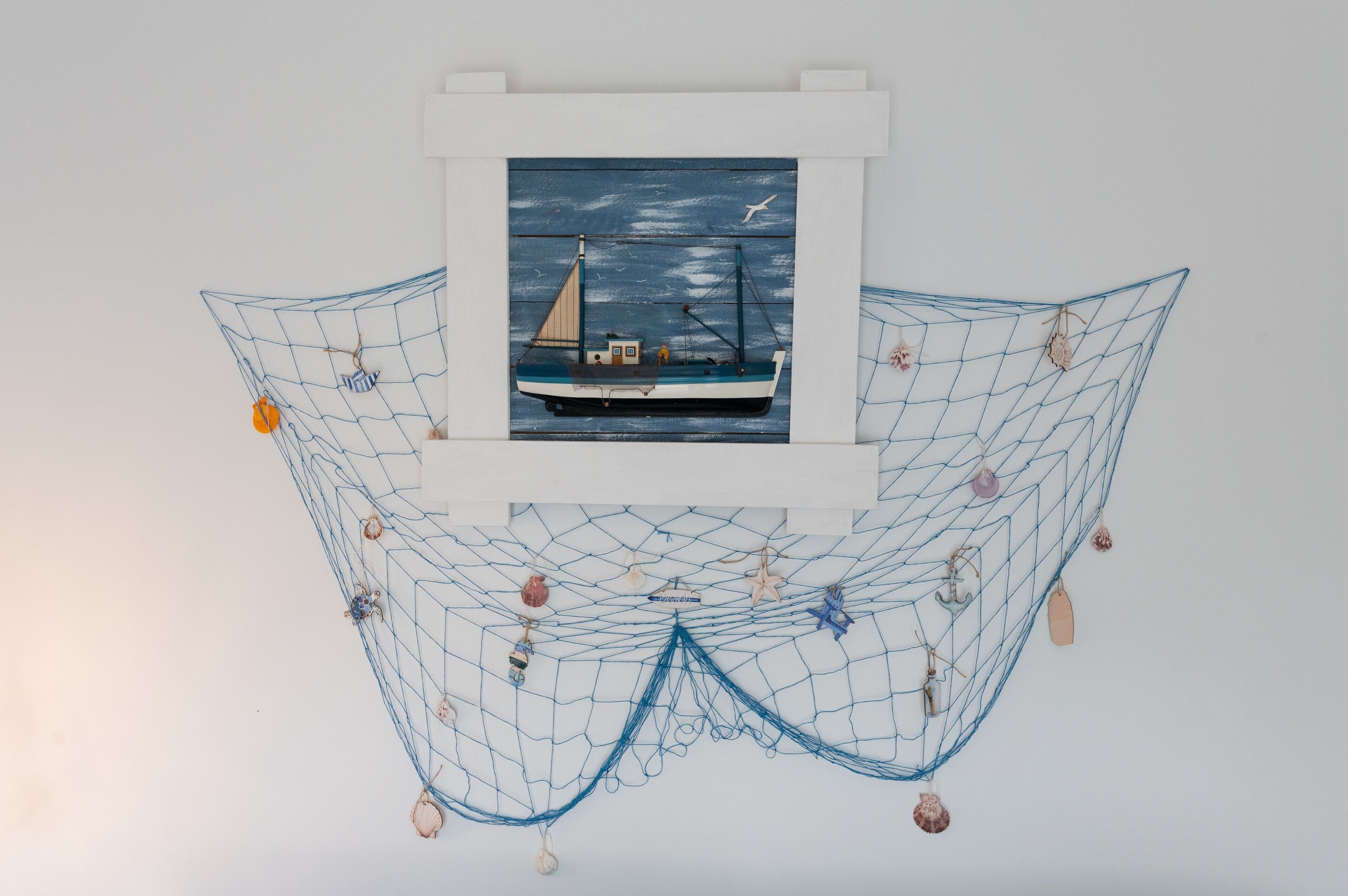 A framed painting of a sailboat on a blue sea, surrounded by a net with seashells and starfish.