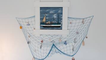 A framed painting of a sailboat on a blue sea, surrounded by a net with seashells and starfish.