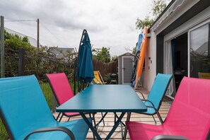 Un patio con mesa y sillas, una zona cubierta para la parrilla y un cobertizo al fondo.