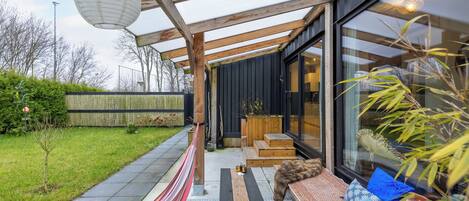 Een moderne buitenruimte met een houten bank, kussens en een hangmat.