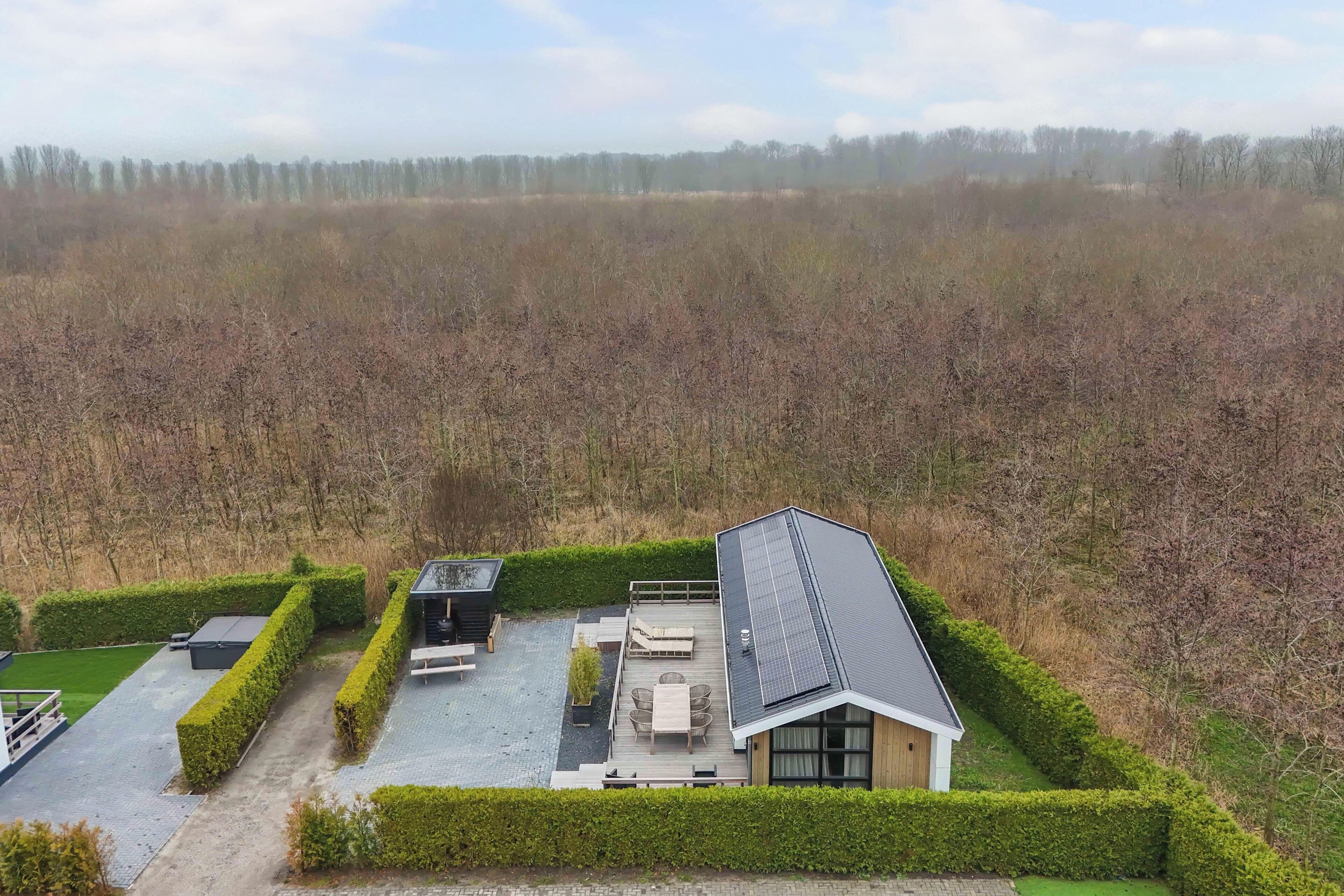 Uma casa moderna com telhado de painéis solares, um pátio com mobiliário externo e um jardim bem cuidado.