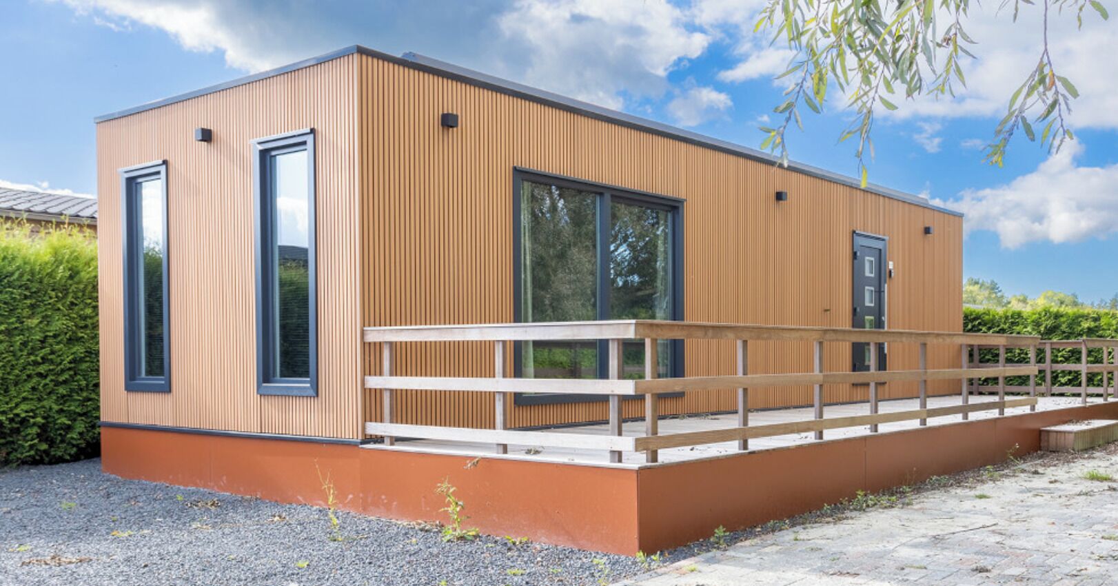 Un edificio moderno con amplios ventanales, una terraza de madera y un techo plano.