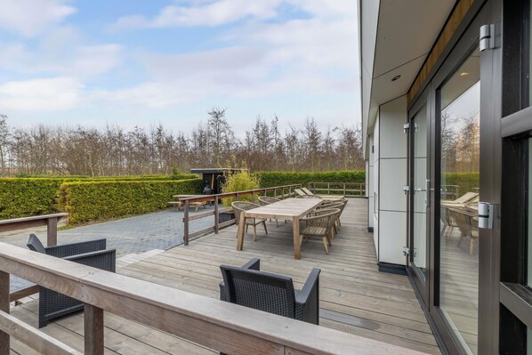 A deck with outdoor furniture, a table, and chairs, overlooking a landscaped area with a hedge and trees. - Vakantiepark In Style (Menaldum)
