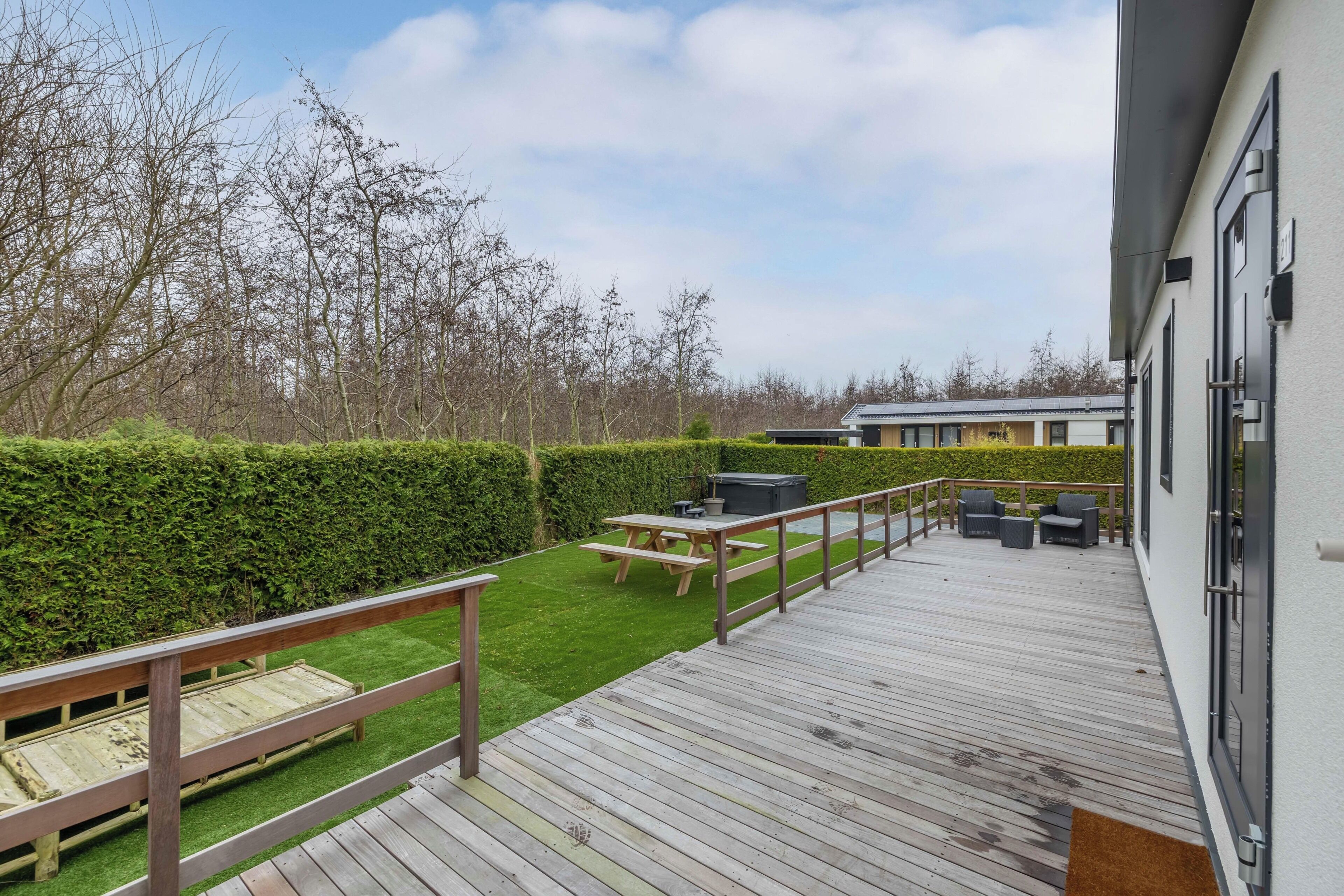 Eine Terrasse mit Picknicktisch und Stühlen, einem Holzzaun und einer Hecke.