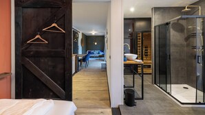 A modern hotel room with a wooden floor, a sliding door with wooden hangers, a glass shower enclosure, and a seating area with a sofa and chairs. - Vakantiepark In Style (Menaldum)