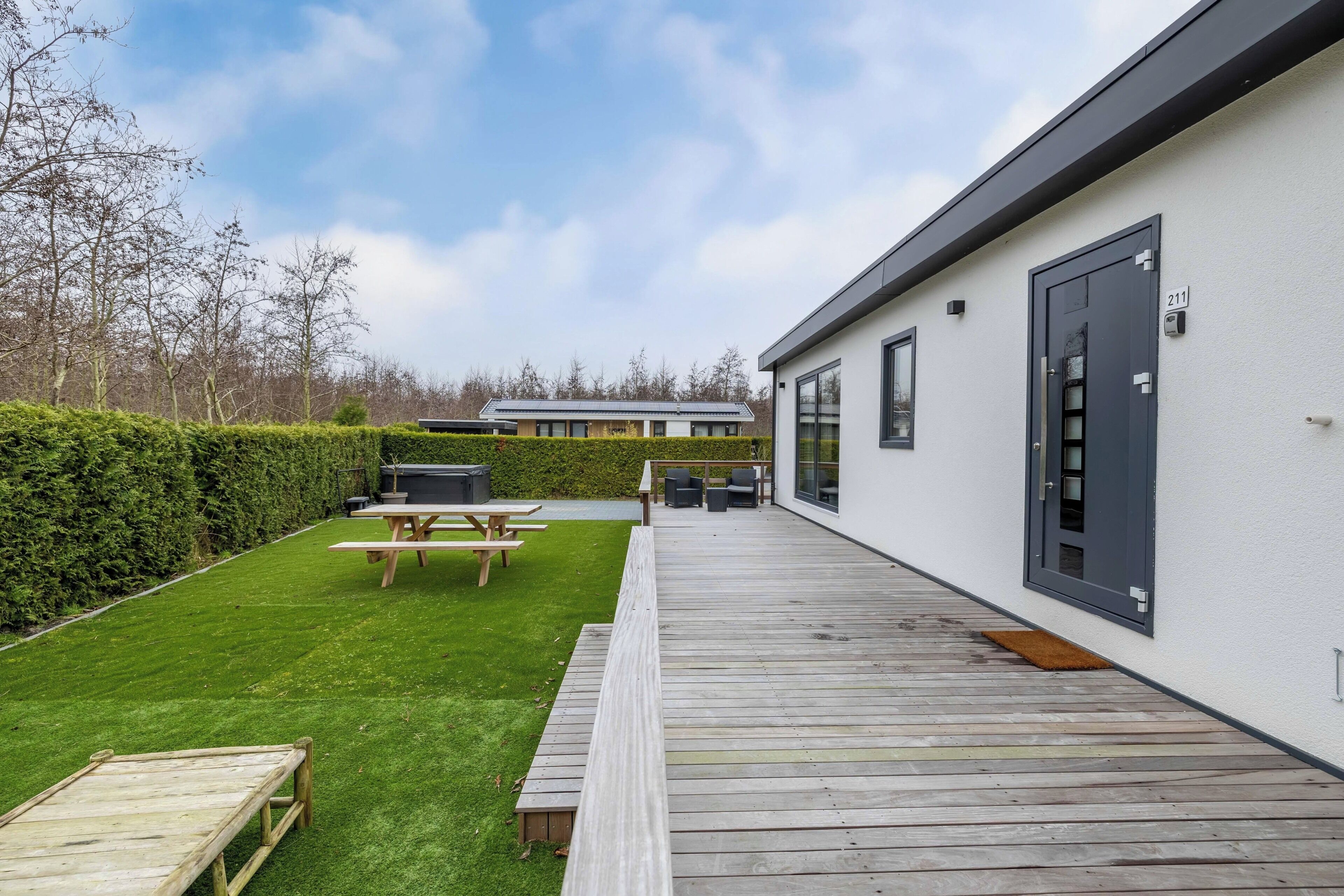 A modern house with a wooden deck, a picnic table, and a barbecue area.