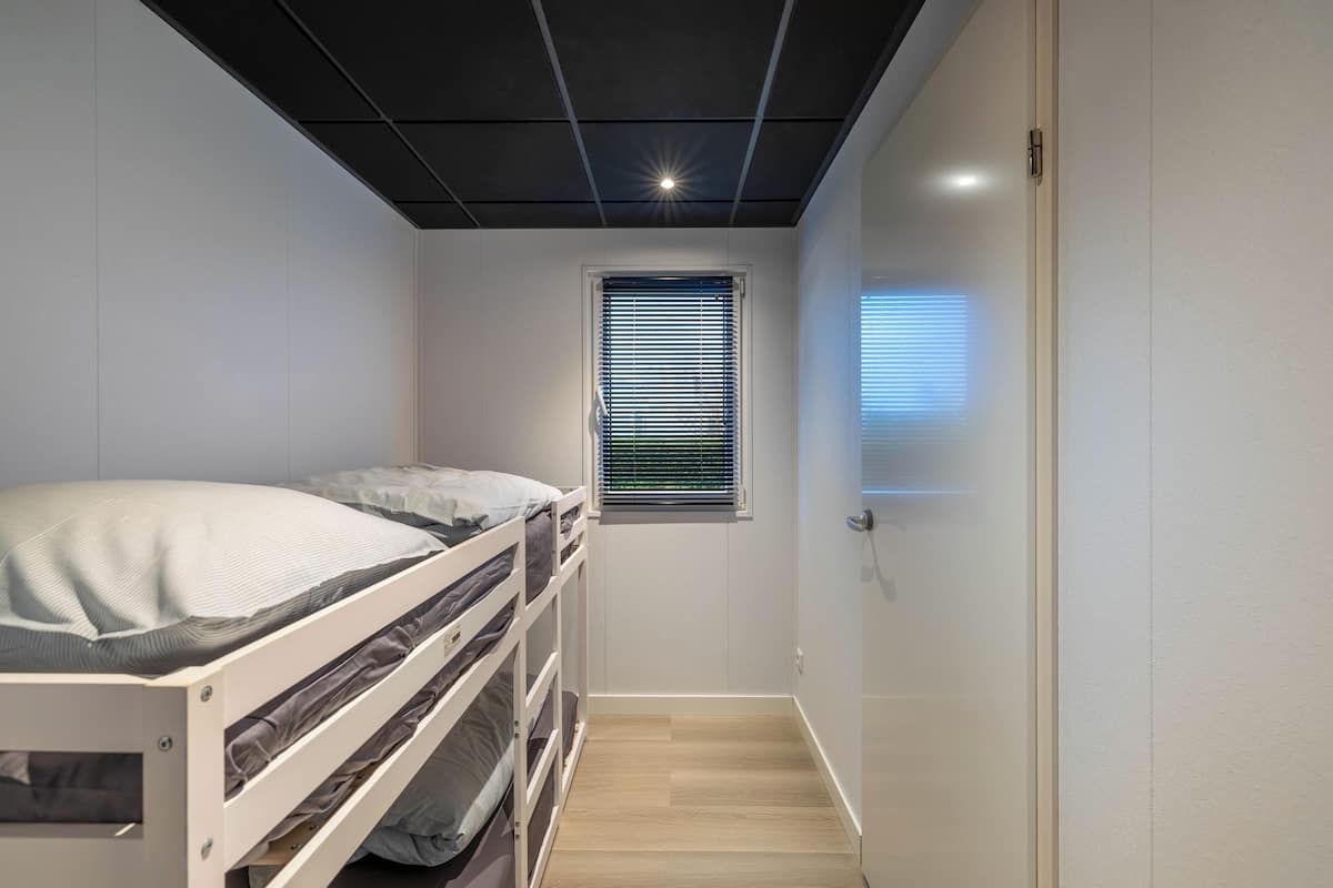 A small, well-lit room with a bunk bed, a window with blinds, and a door.