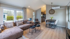 A modern living room with a sectional sofa, a dining table with chairs, a hanging light fixture, and a kitchen area in the background. - Vakantiepark In Style (Menaldum)
