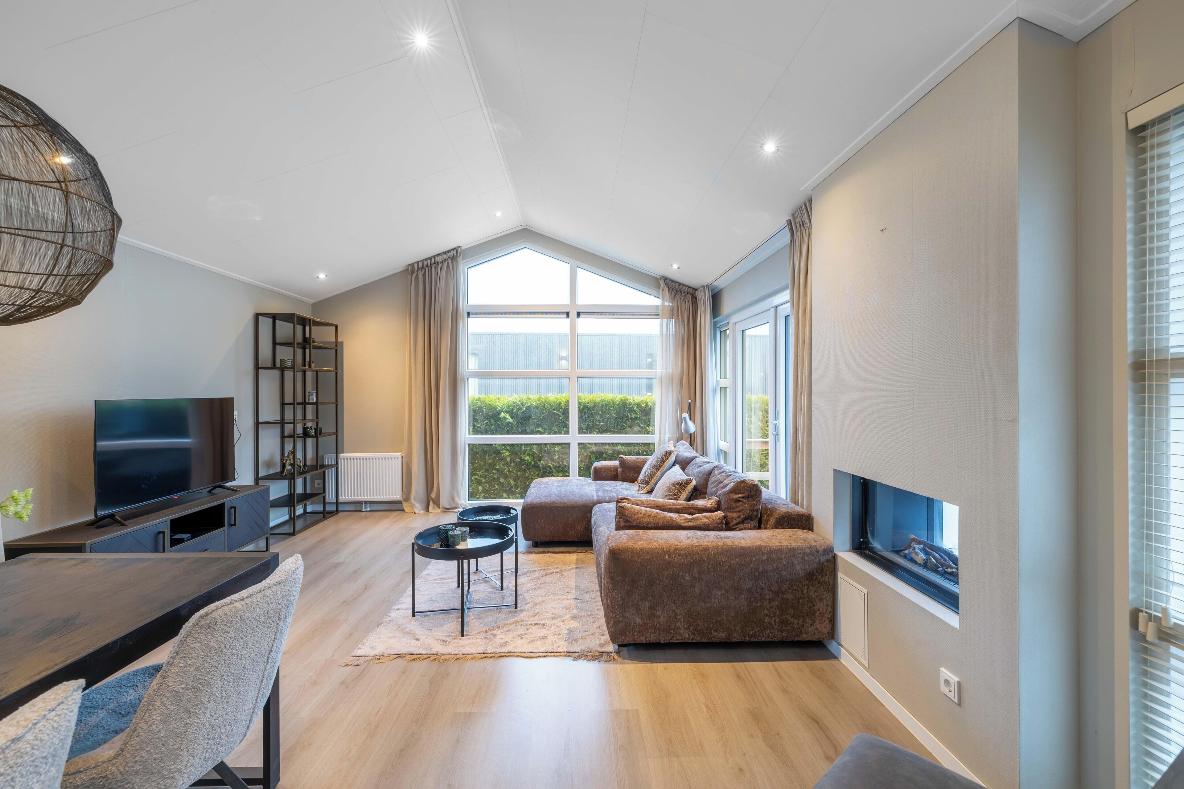 A modern living room with a TV, sofa, and large windows.