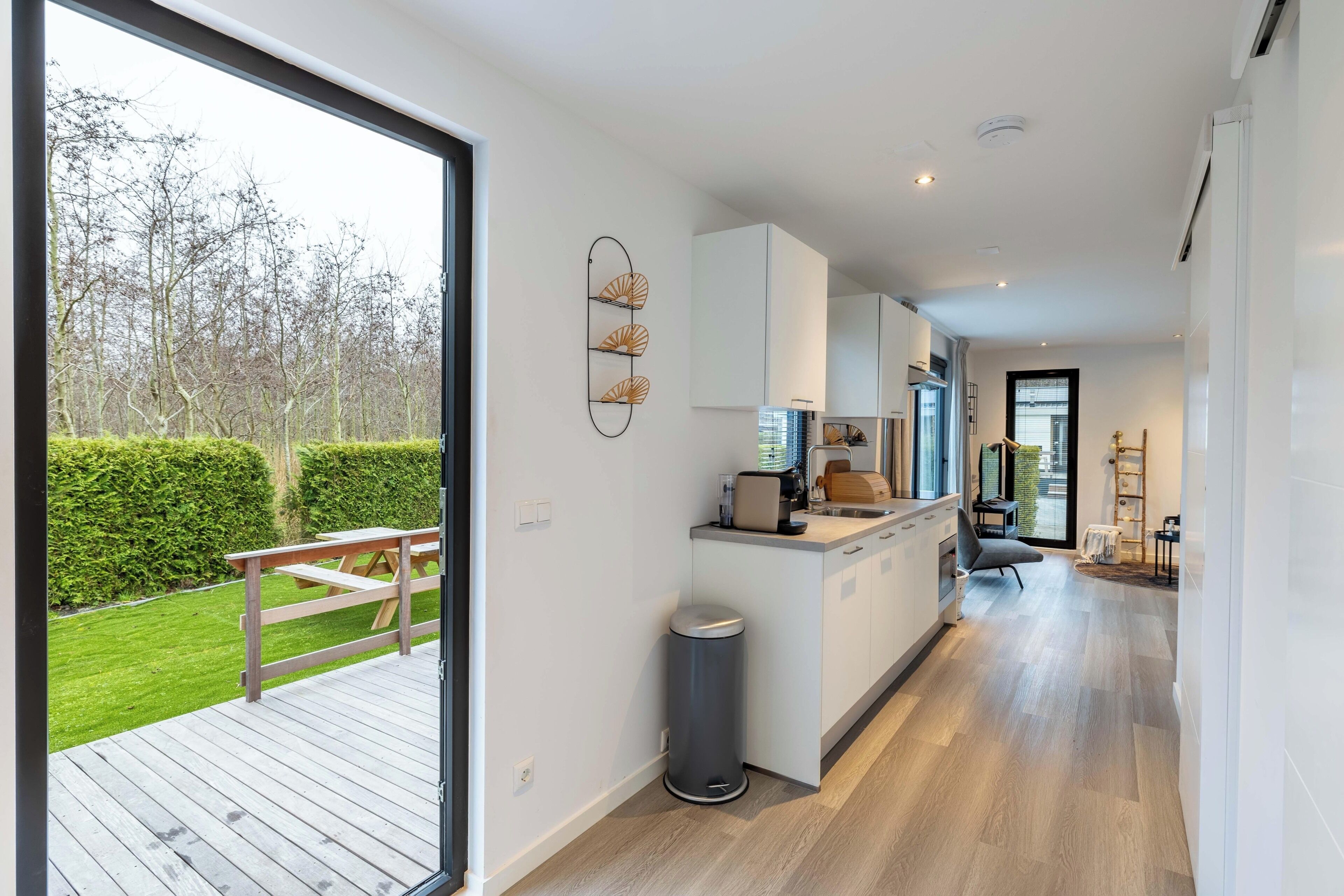 A modern kitchen with a view of the outdoors, a trash bin, and a wooden deck.