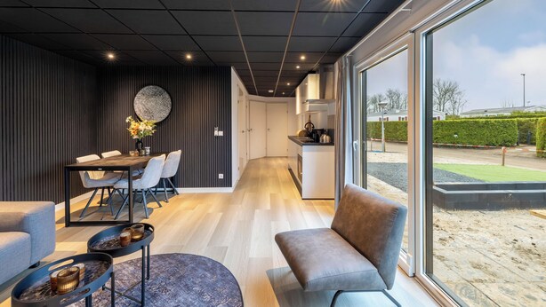 A modern interior with a dining area, a kitchen, and a large window offering a view of the outdoors. - Vakantiepark In Style (Menaldum)