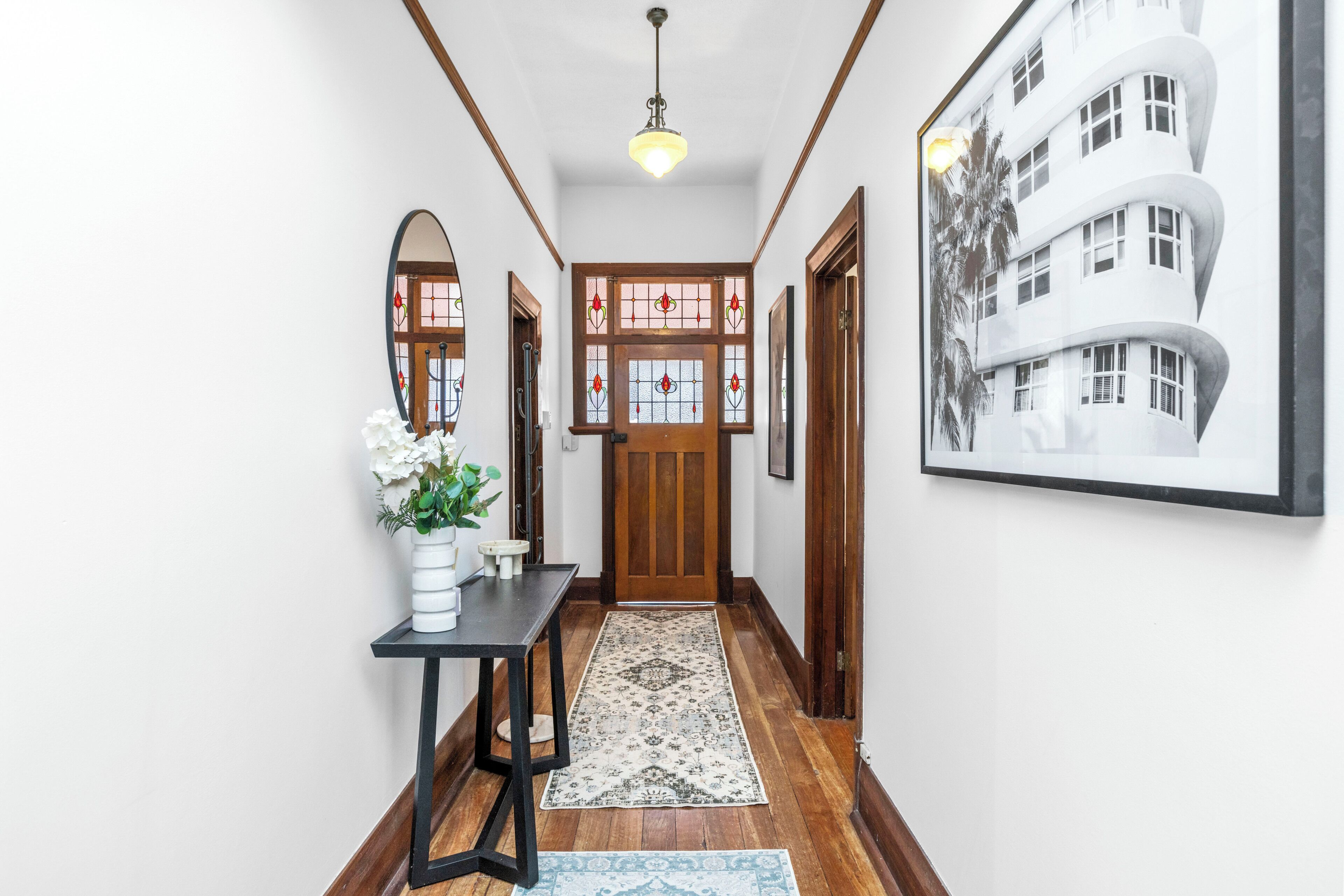 A hallway with a wooden door, a black table with a vase, and a patterned rug.